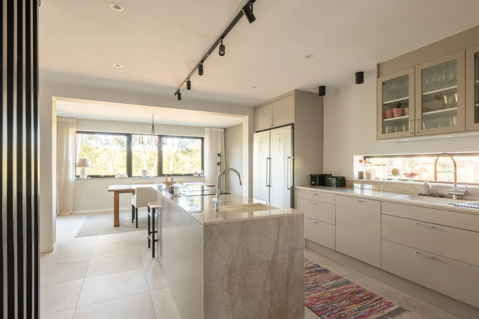 Interiör av ett ljust kök med en köksö i sten. Minimalistisk design och en öppen planlösning som leder vidare in i bostaden.